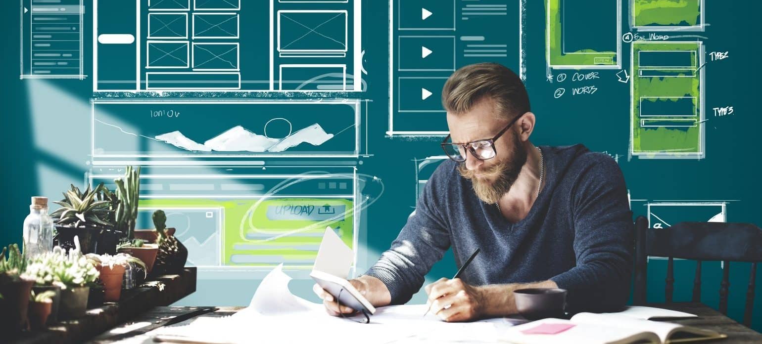 Man at desk in front of chalk board holding notebook taking notes